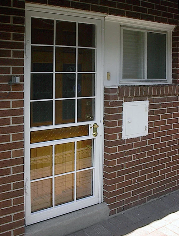 White security screen door installed on the brick front entrance of a residential home